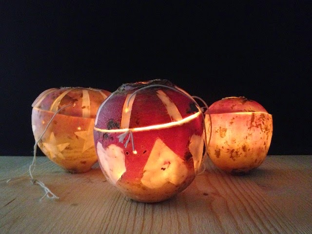 Three carved illuminated lanterns made from hollowed fruit with cut-out star and triangle patterns, glowing warmly on a dark surface